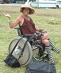 Photo:  Smiling woman in a sun hat, sitting in a wheelchair in a field, just after taking down her tent at a three-day festival.